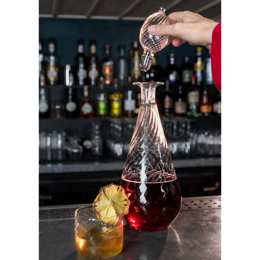 Person pouring a drink from a glass decanter into a glass with a bar setting in the background., Nabucho Wine Carafe – Mouth-Blown Borosilicate Glass – Maison Holder