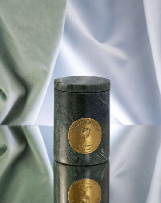 Marble cylindrical container with gold emblem on a reflective surface, Tindari Marble Candle – Venetico Marina – Maison Holder
