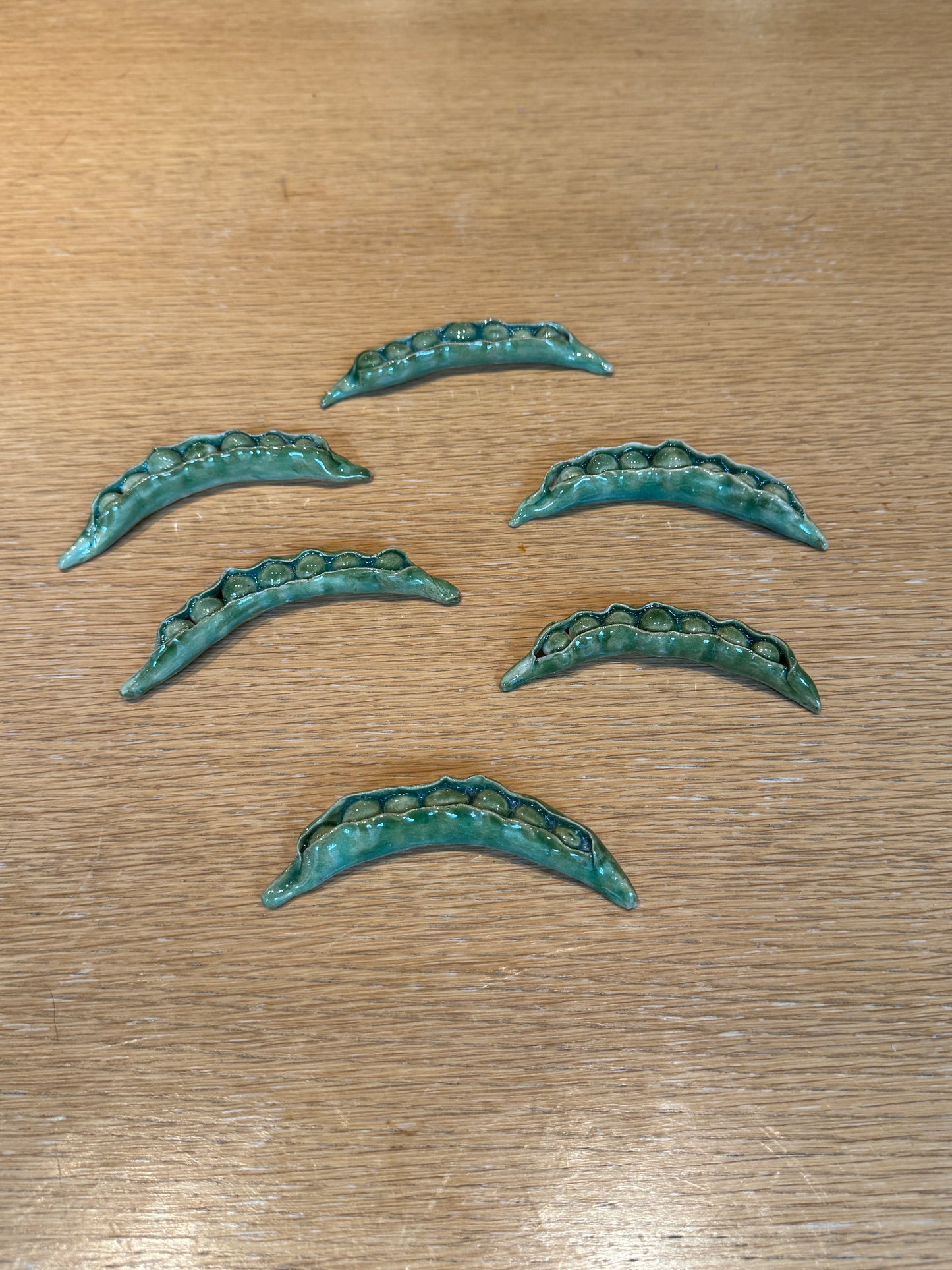 Set of six green metallic decorative elements on a wooden surface, Peas Knife Rest – Handmade Ceramic – Nathalie Reignault Sann