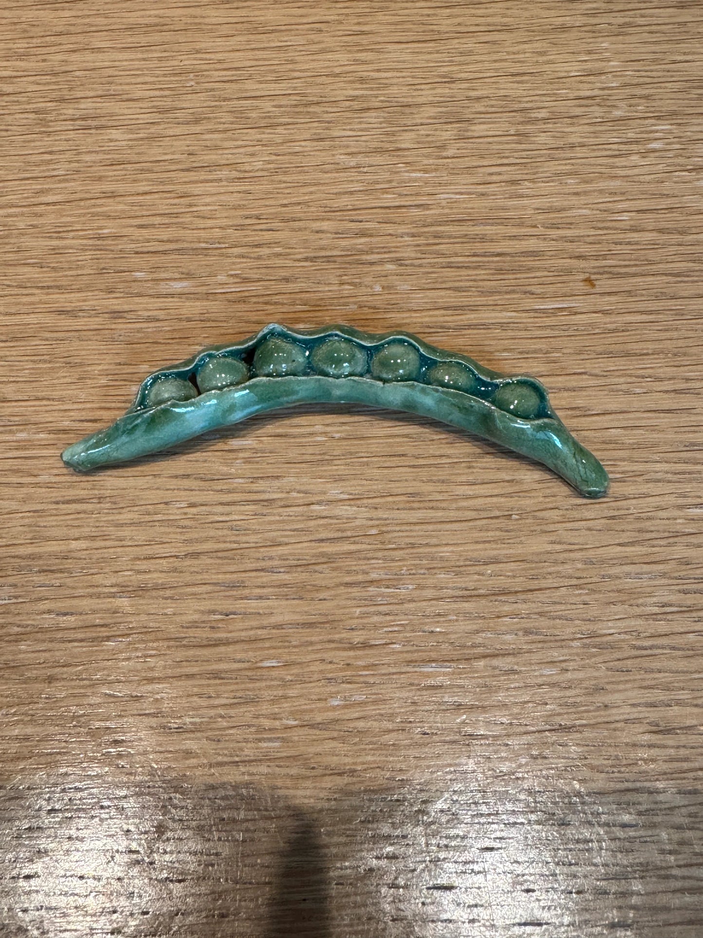 Bronze decorative item shaped like a leaf on a wooden surface, Peas Knife Rest – Handmade Ceramic – Nathalie Reignault Sann