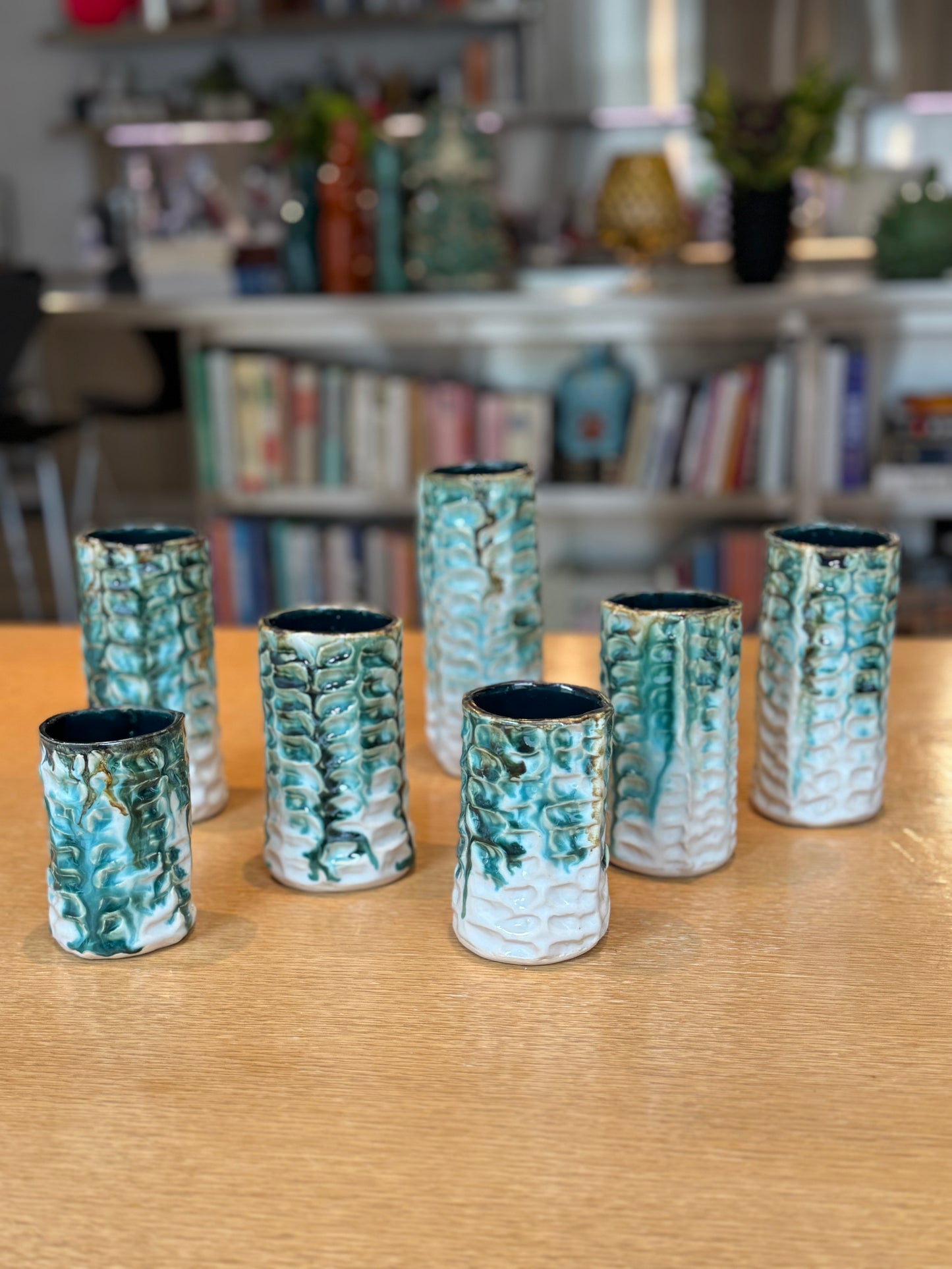 Set of ceramic vases with textured design on a wooden surface, with a blurred background of books and decor. Vases Coraux Handmade Ceramic - Nathalie Reignault Sann
