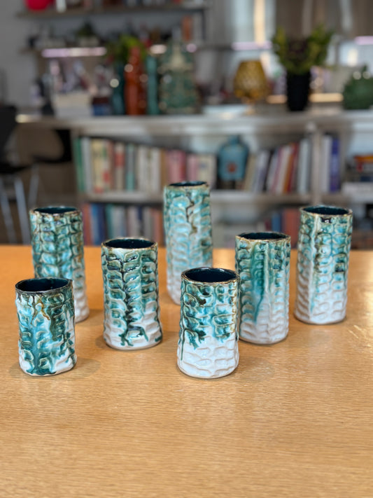 Set of ceramic vases with textured design on a wooden surface, with a blurred background of books and decor. Vases Coraux Handmade Ceramic - Nathalie Reignault Sann