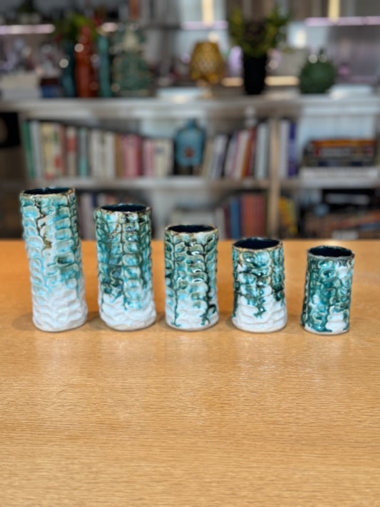 Five ceramic vases with textured design on a wooden surface, blurred background of books and decor. Vases Coraux Handmade Ceramic - Nathalie Reignault Sann