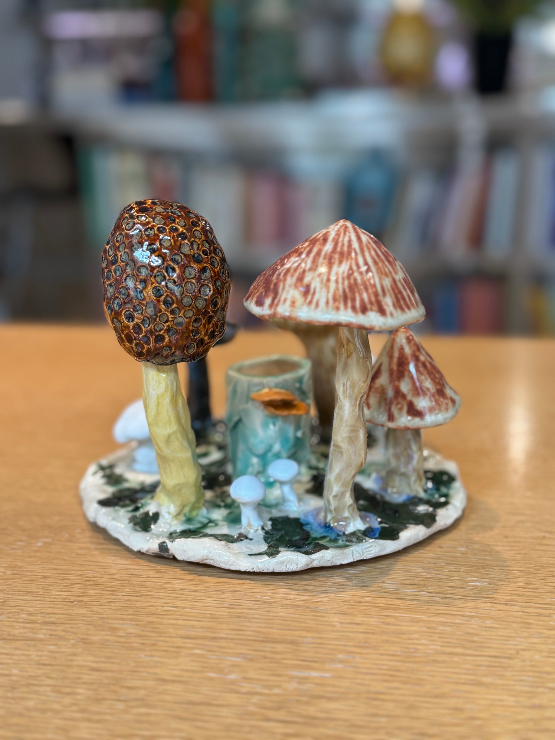 Decorative mushroom figurine on a wooden surface with a blurred bookshelf background, Mushroom Candles – Handmade Ceramic – Nathalie Reignault Sann