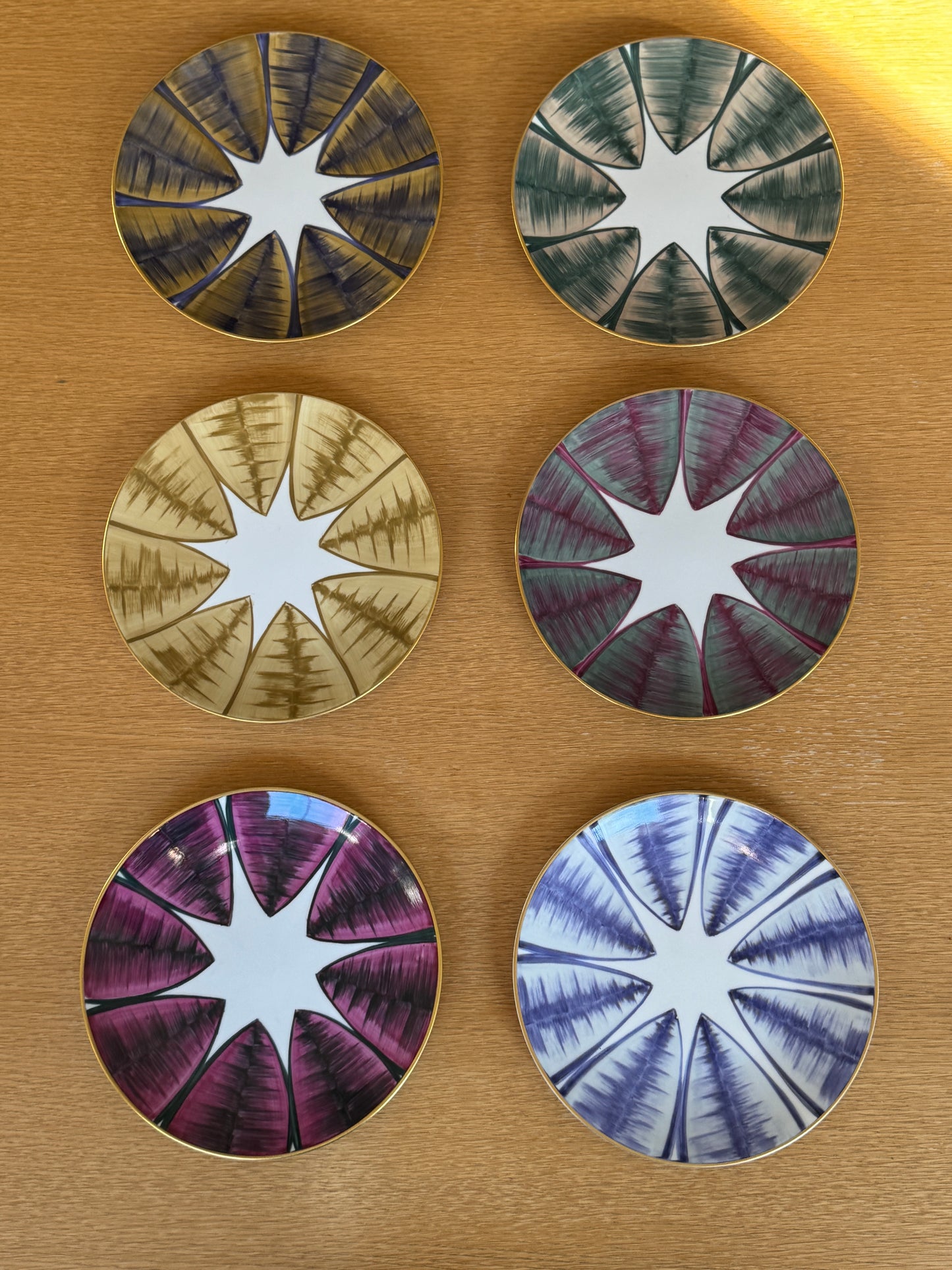 Five circular plates with starburst patterns on a wooden surface, Agave Hand-Painted Dessert Plate – Porcelain – Marie Daâge