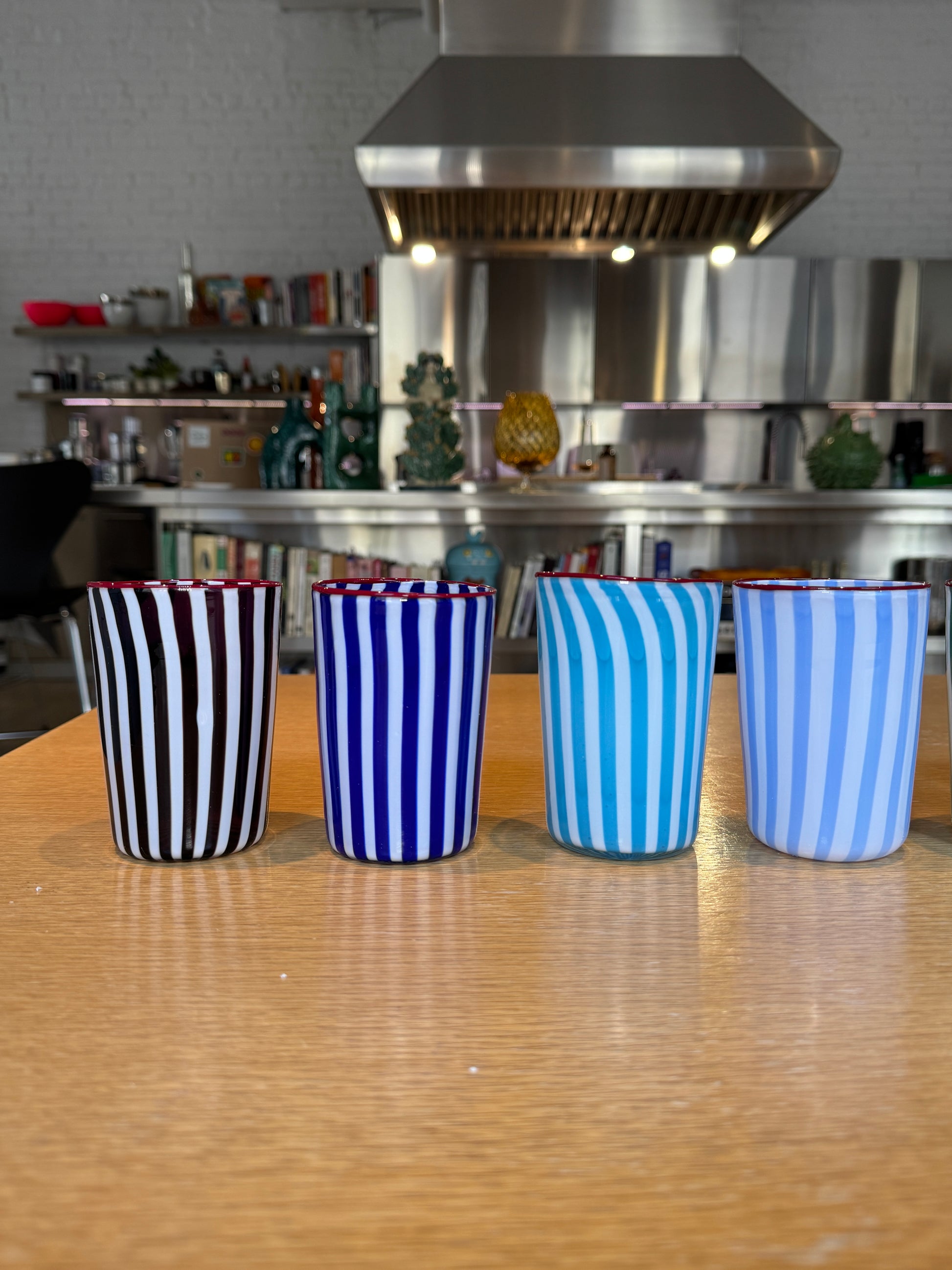 Striped cups on a wooden surface with a metallic appliance in the background Joyful Stripe Glasses – Murano Cane Glassware – Maison Holder