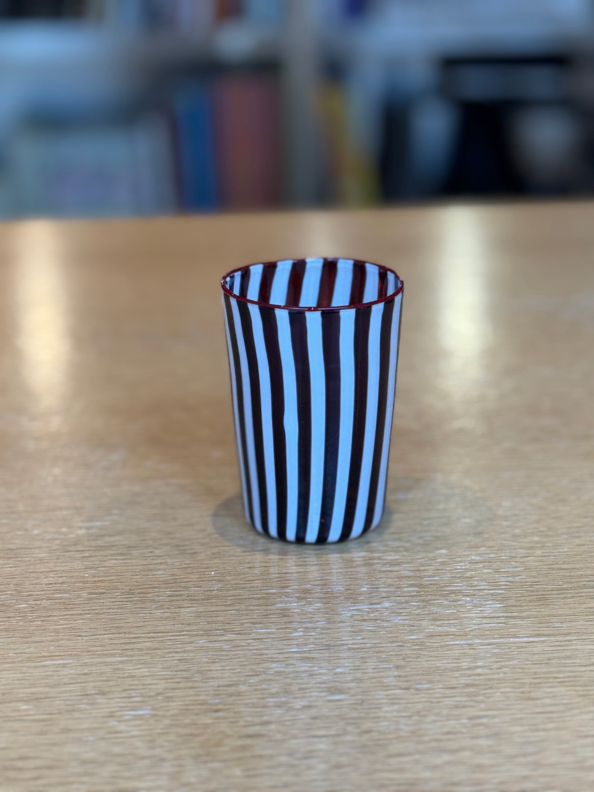 Striped glass cup on a wooden surface with a blurred background, Joyful Stripe Glasses – Murano Cane Glassware – Maison Holder