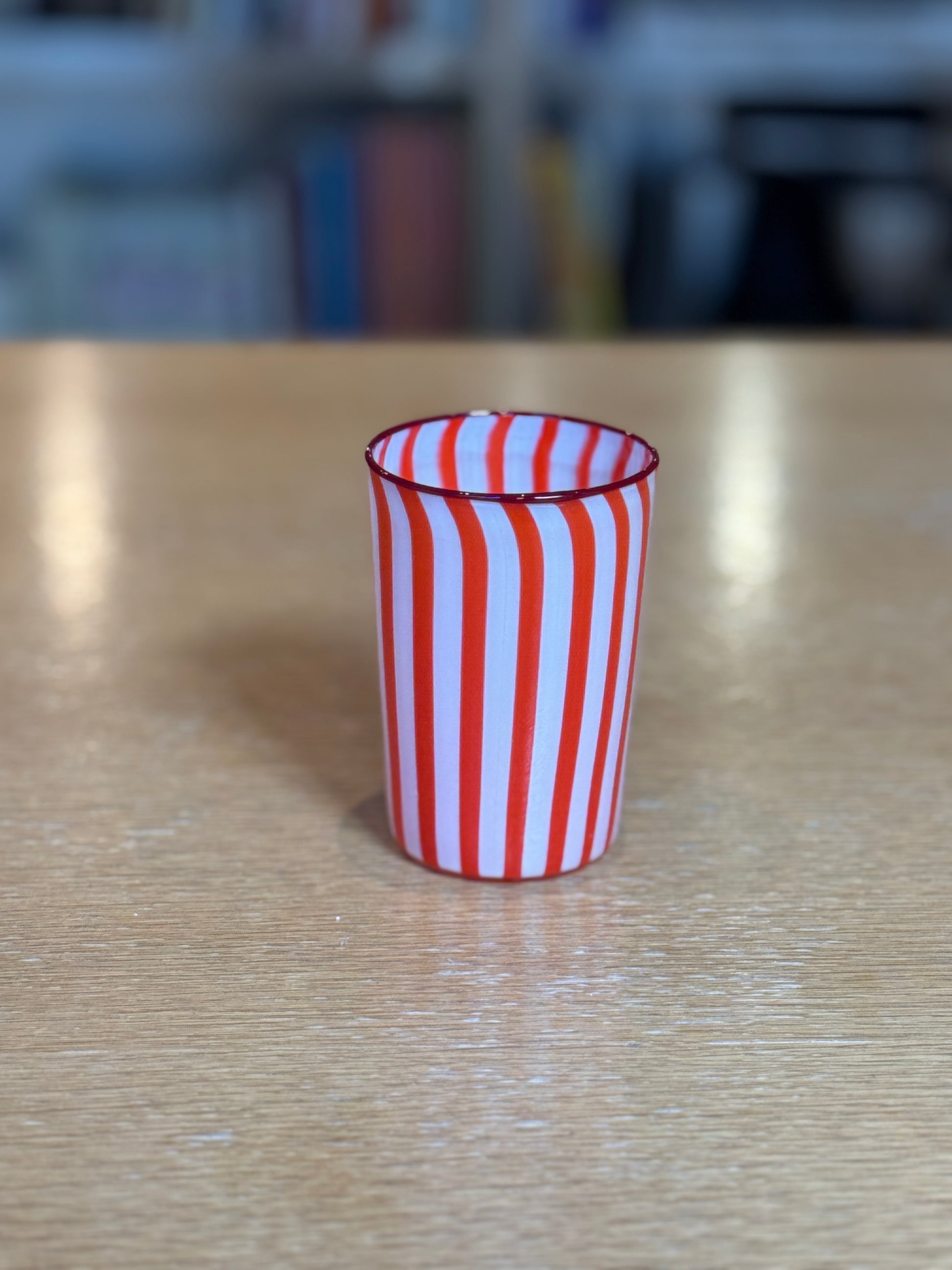 Red and white striped glass on a wooden table with a blurred background Joyful Stripe Glasses – Murano Cane Glassware – Maison Holder