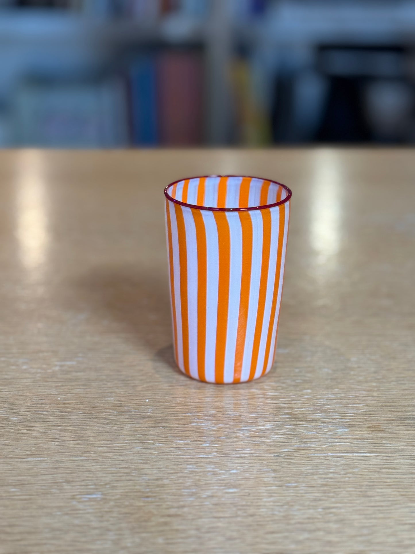 Striped glass cup on a wooden surface with a blurred background, Joyful Stripe Glasses – Murano Cane Glassware – Maison Holder