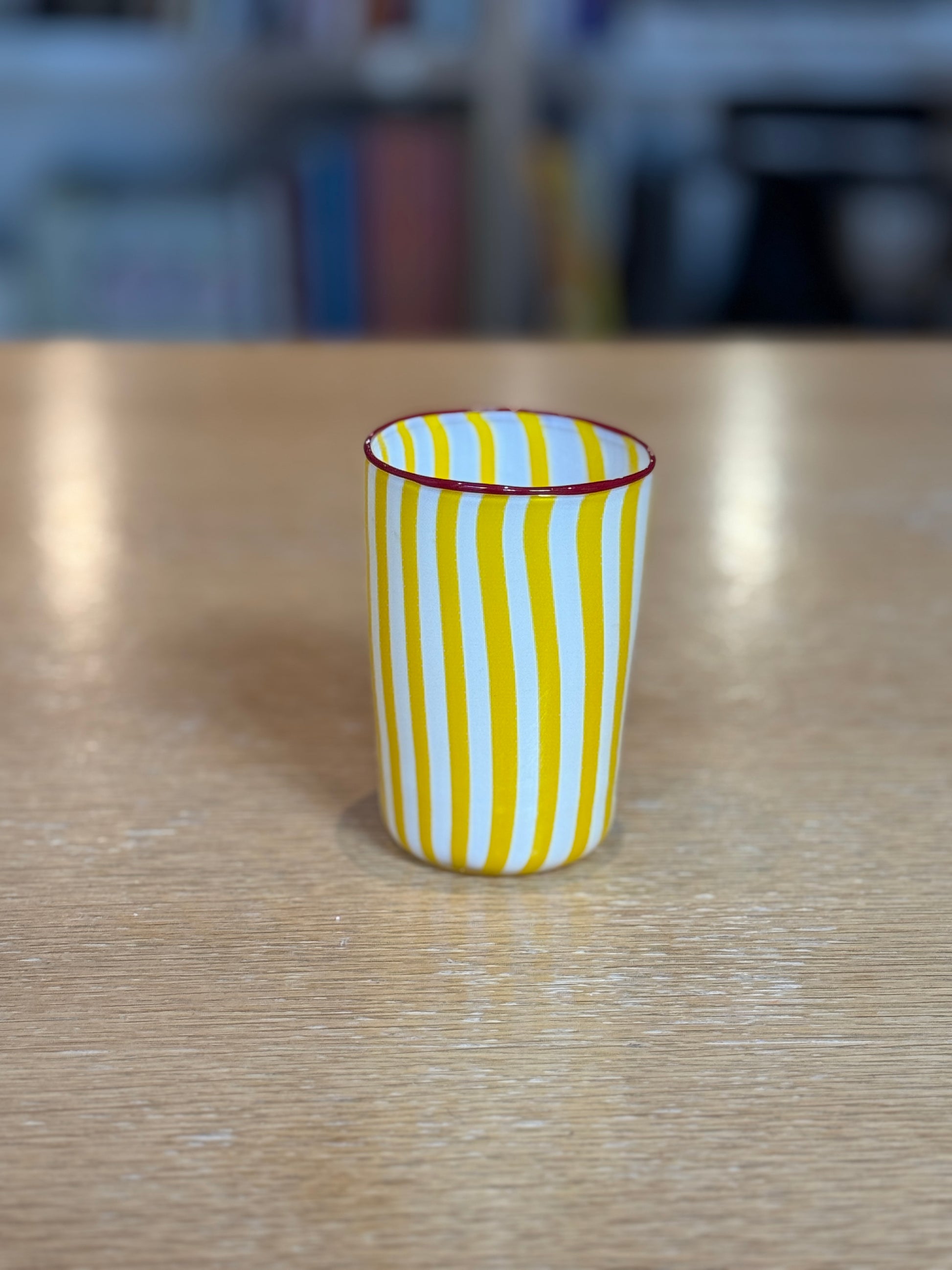 Striped glass cup on a wooden surface with a blurred background, Joyful Stripe Glasses – Murano Cane Glassware – Maison Holder