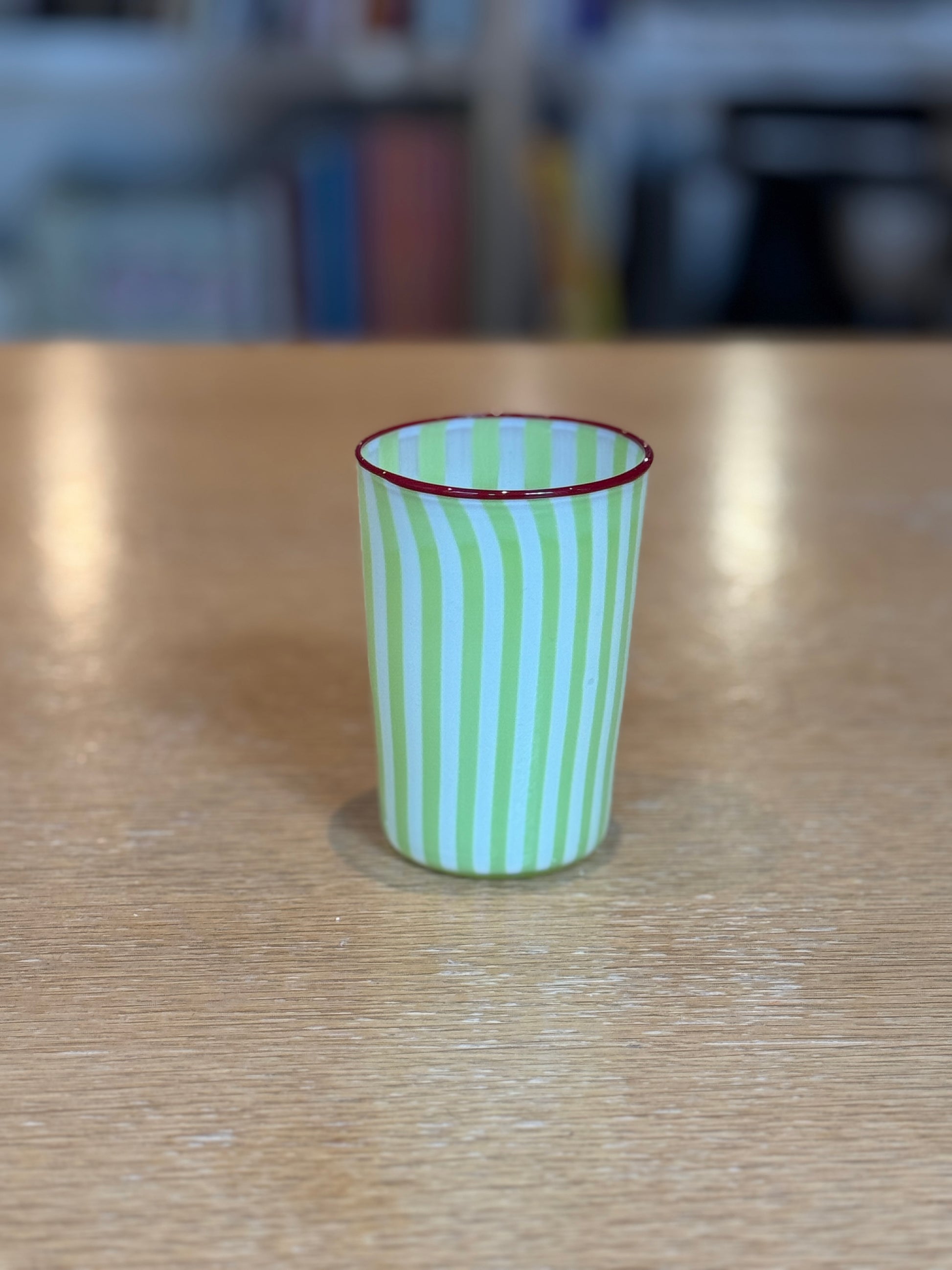 Green and red striped glass on a wooden surface with a blurred background Joyful Stripe Glasses – Murano Cane Glassware – Maison Holder