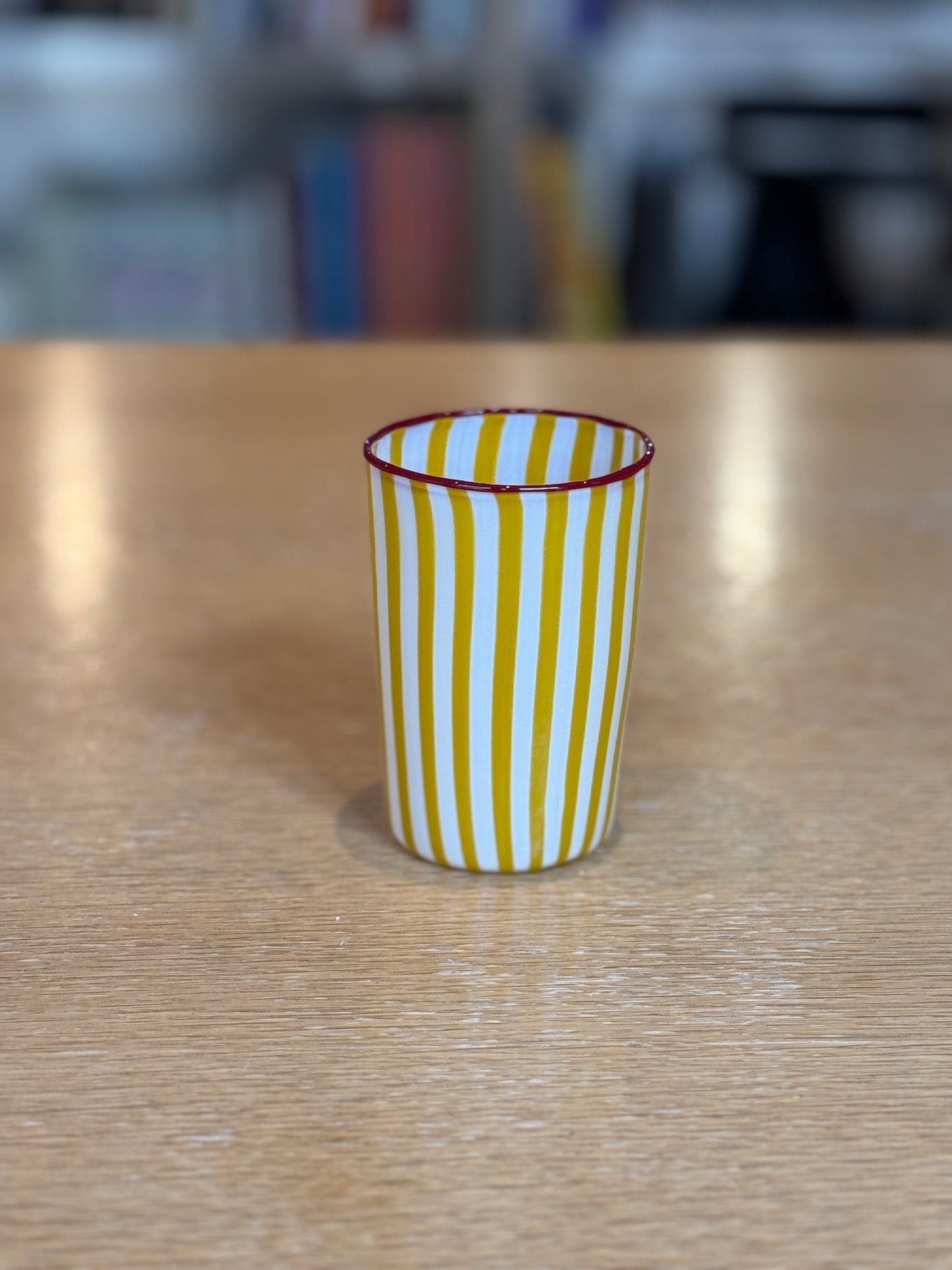 Yellow and white striped cup on a wooden table with a blurred background, Joyful Stripe Glasses – Murano Cane Glassware – Maison Holder
