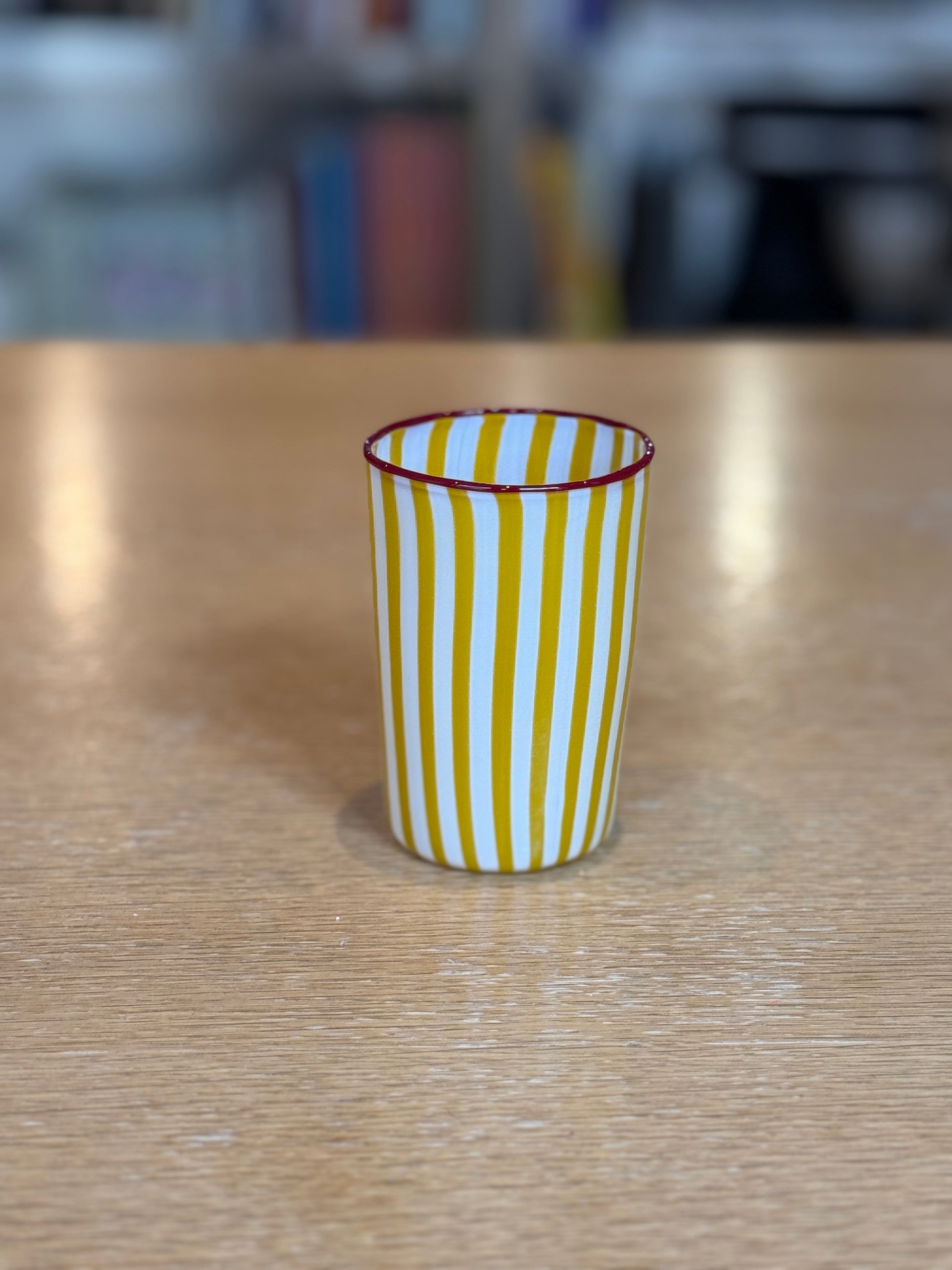Yellow and white striped cup on a wooden table with a blurred background, Joyful Stripe Glasses – Murano Cane Glassware – Maison Holder