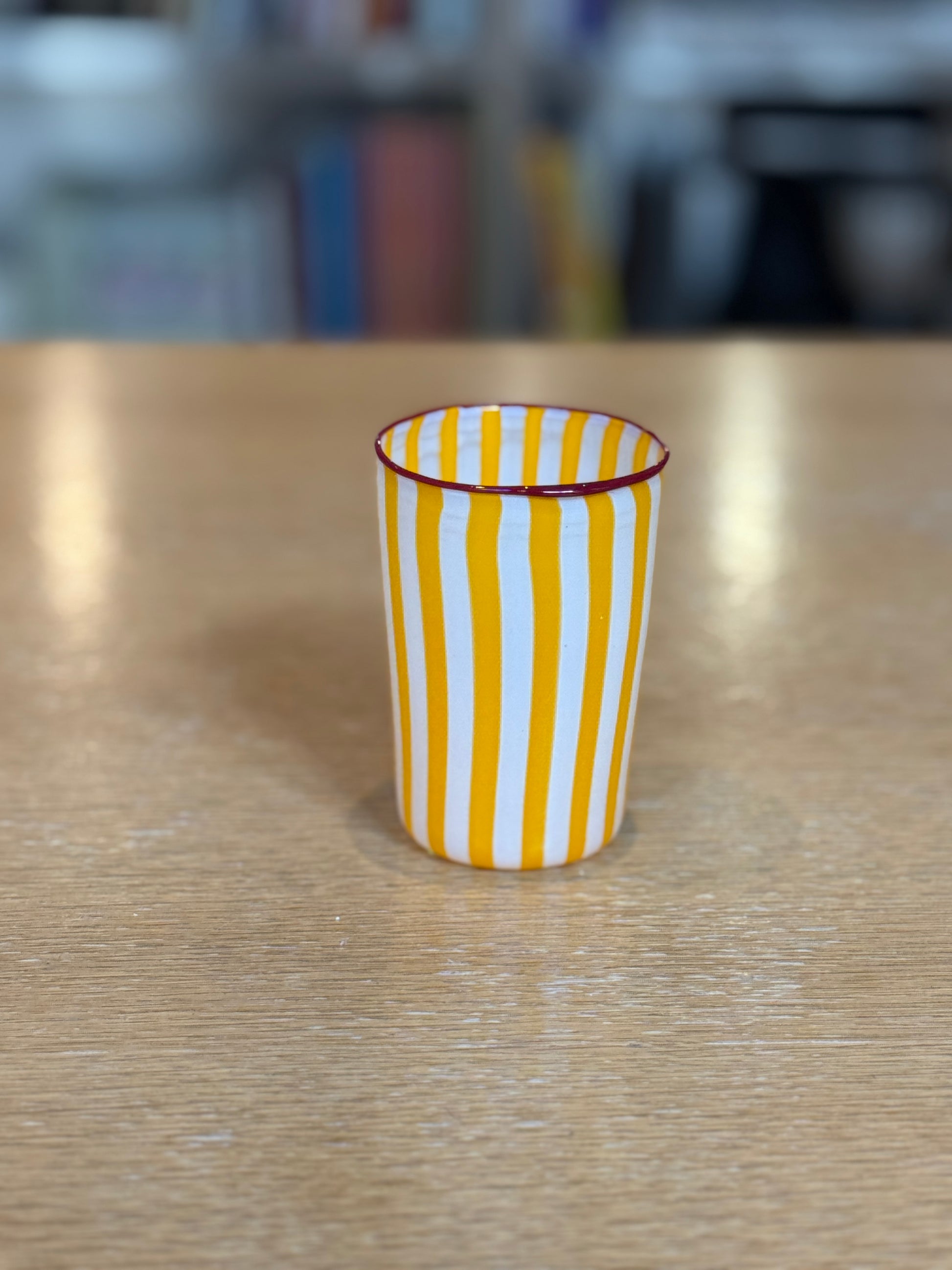 Yellow and white striped glass on a wooden surface with a blurred background, Joyful Stripe Glasses – Murano Cane Glassware – Maison Holder