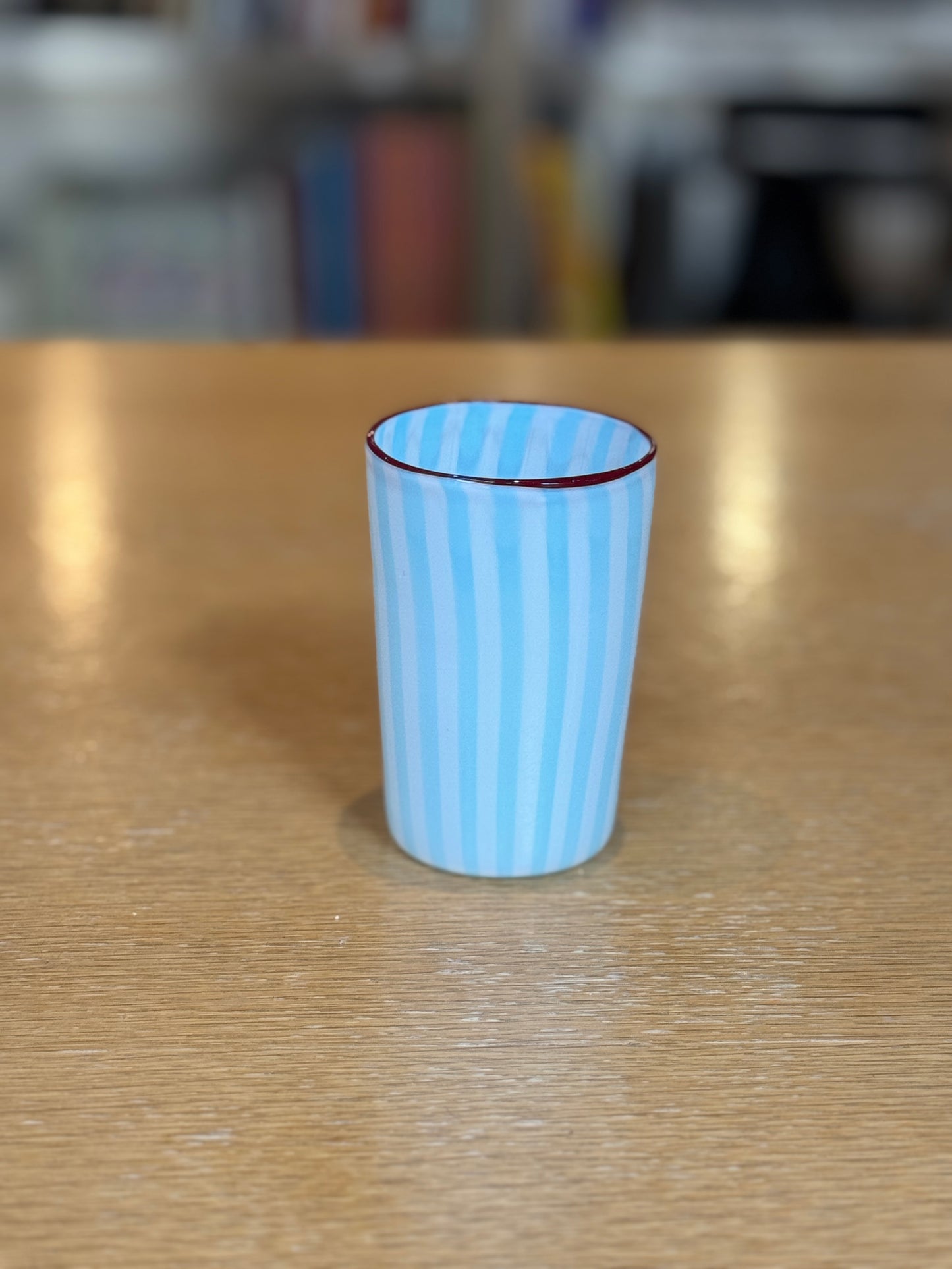 Blue striped cup on a wooden surface with a blurred background, Joyful Stripe Glasses – Murano Cane Glassware – Maison Holder