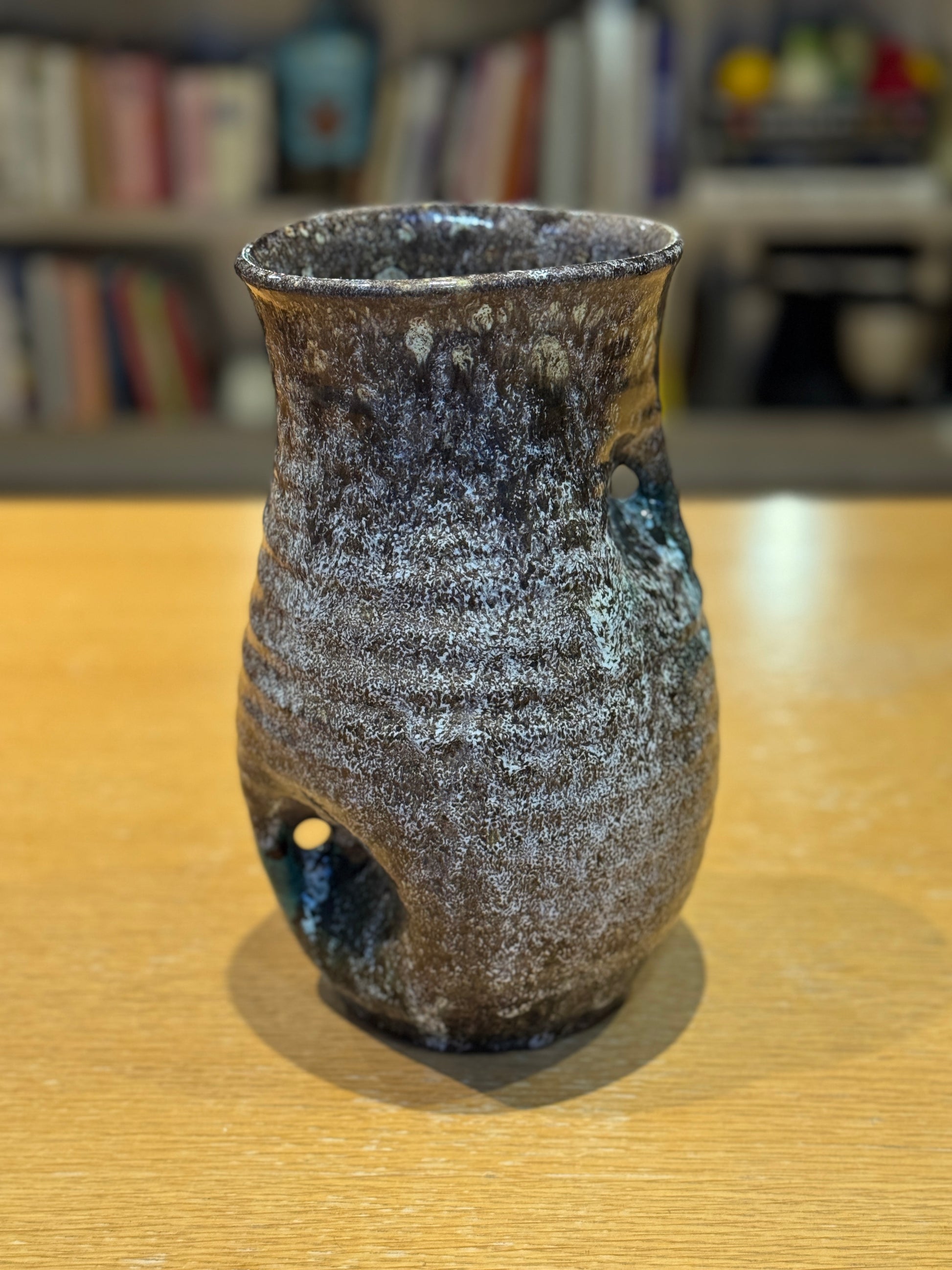 Vintage Vase - Accolay 1960s, Speckled brown and black ceramic vase on a wooden surface with a blurred bookshelf background