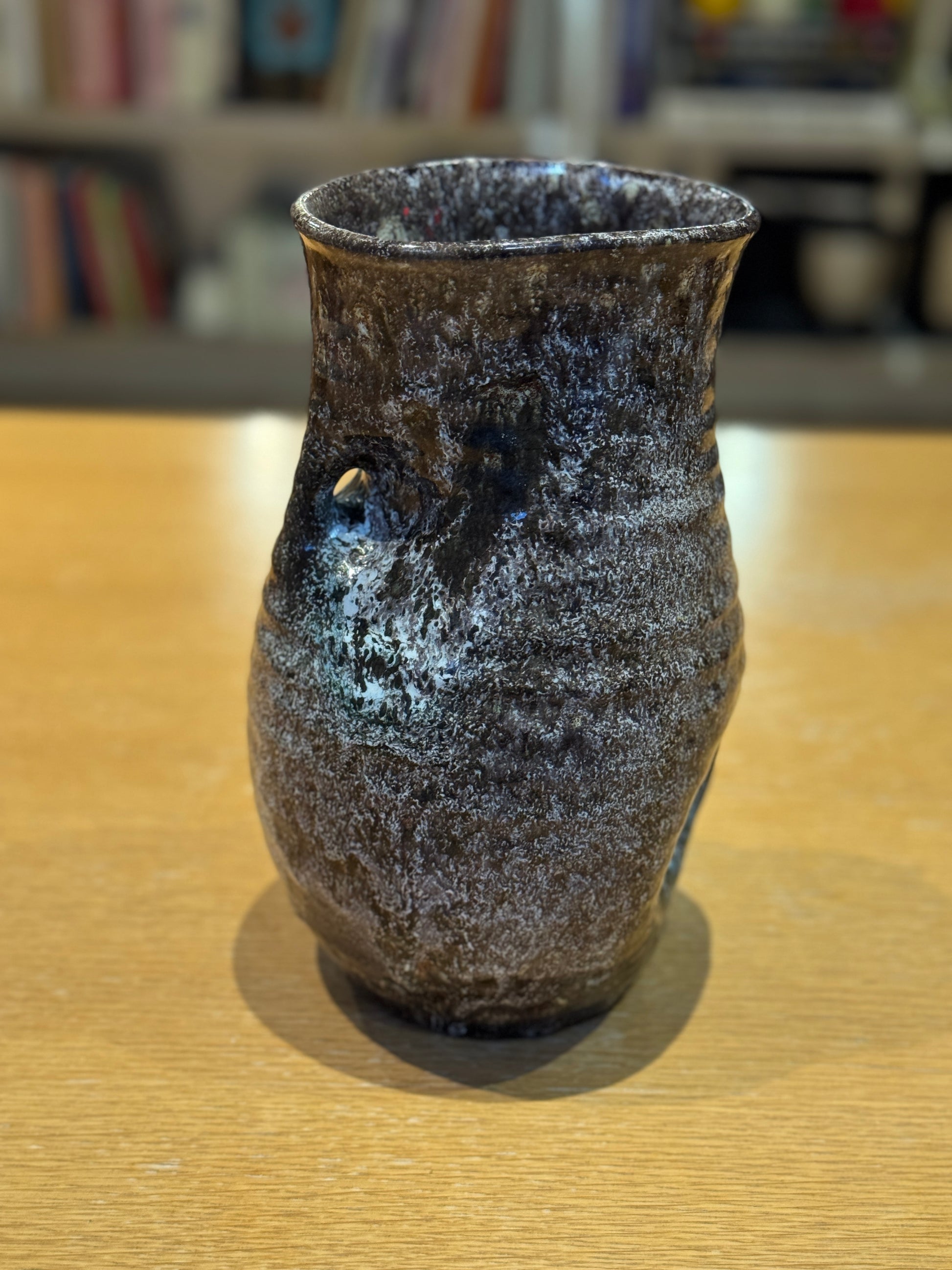 Vintage Vase - Accolay 1960s, Speckled brown and black ceramic vase on a wooden surface with a blurred bookshelf background