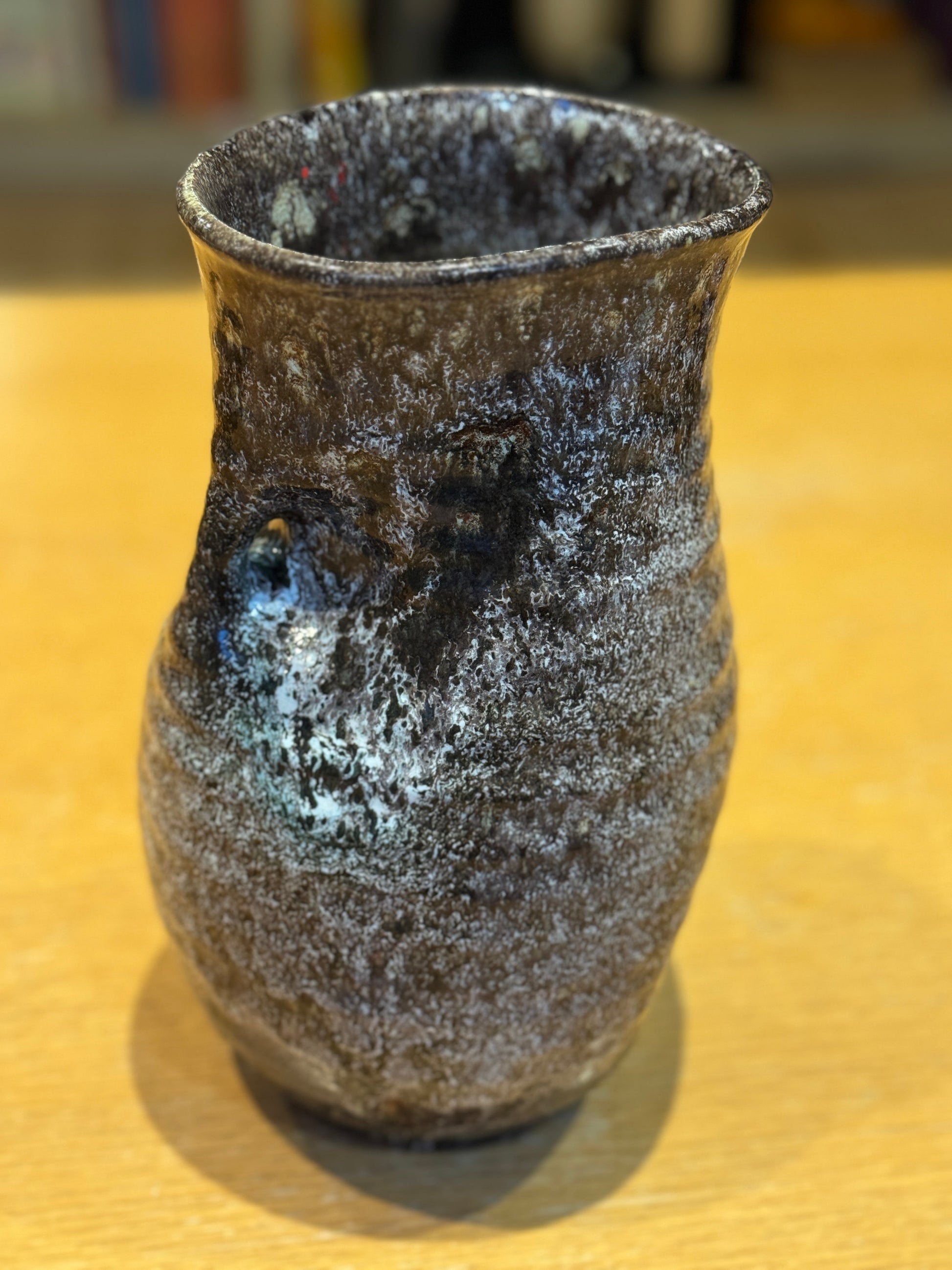 Vintage Vase - Accolay 1960s, Speckled brown and black ceramic vase on a wooden surface with a blurred bookshelf background
