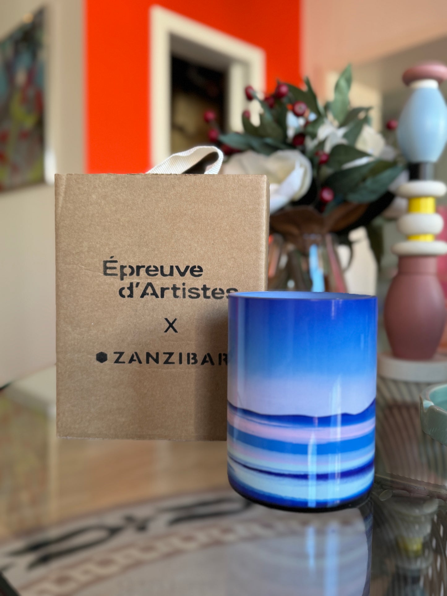 Blue glass candle with 'Épreuve d'Artistes x Zanzibar' packaging on a reflective surface. Tanc Large Candle – Épreuve d’Artistes – Maison Holder