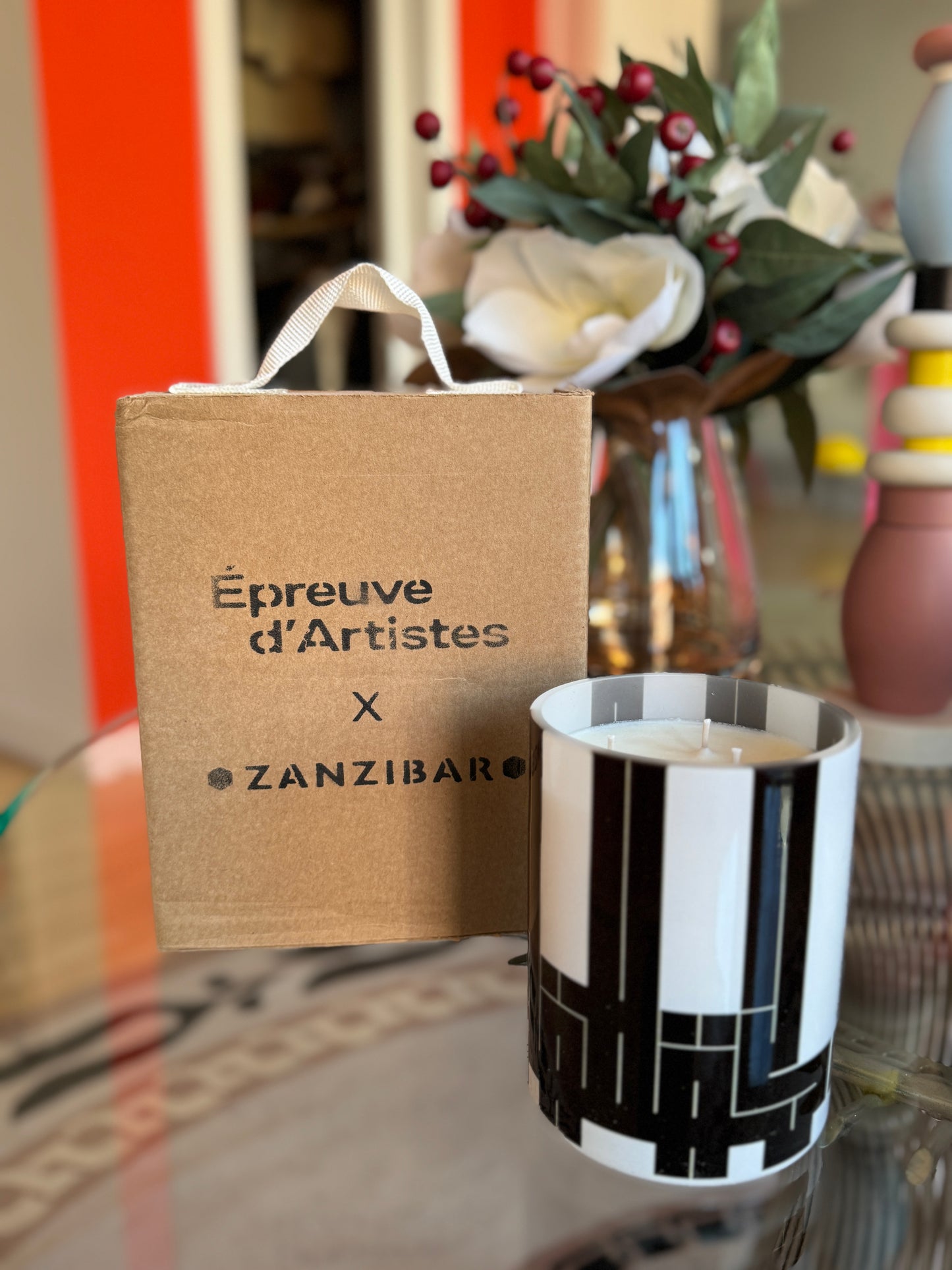 Black and white striped candle with 'Epreuve d'Artistes x Zanzibar' packaging on a reflective surface. L’Atlas Large Candle – Épreuve d’Artistes – Maison Holder