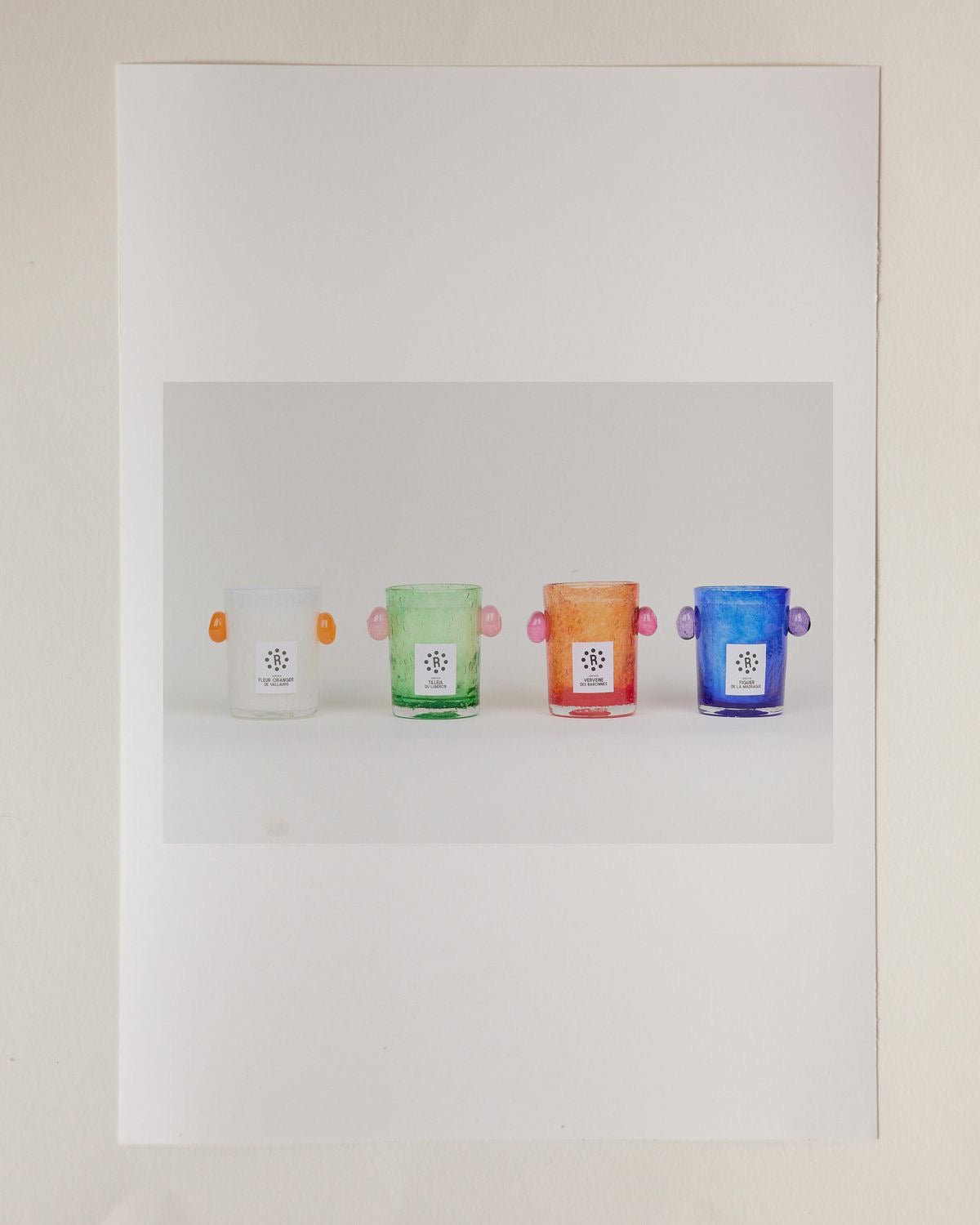 Four colorful glass containers with handles on a white background, Peony Candle Luberon Lime Blossom – La Romaine Editions – Maison Holder