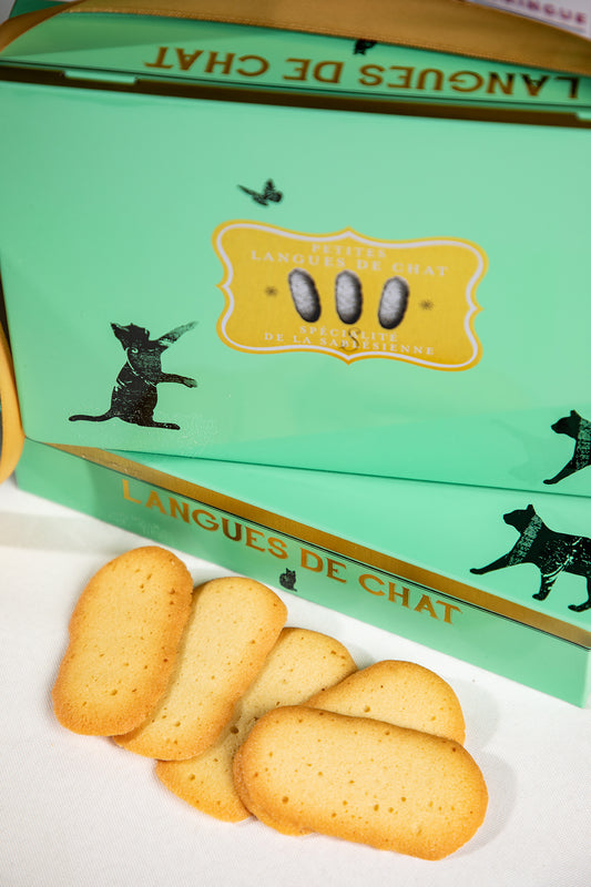 Biscuits in front of a green box labeled 'Langues de Chat' on a white surface. Cat’s Tongue Tin – Classic French “Langue de Chat” – Maison Holder