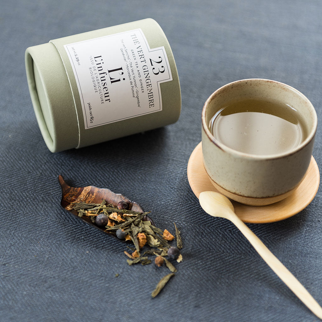 Tea canister, cup with tea leaves, and wooden spoon on a dark surface, Organic Ginger Green Tea N°23 by L'Infuseur – Antioxidant Blend