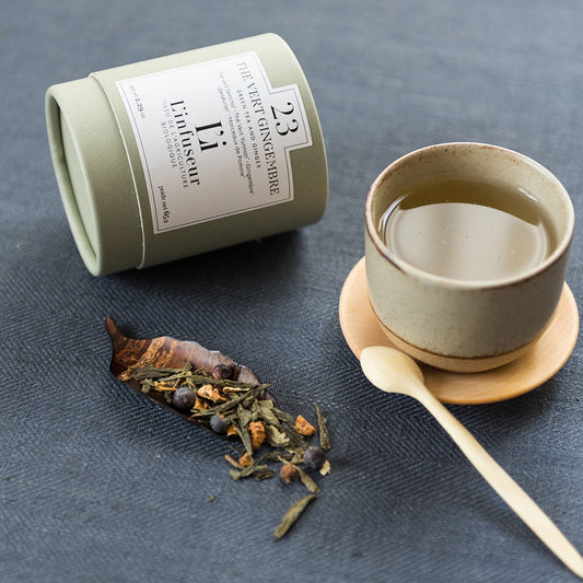 Tea canister, cup with tea leaves, and wooden spoon on a dark surface, Organic Ginger Green Tea N°23 by L'Infuseur – Antioxidant Blend