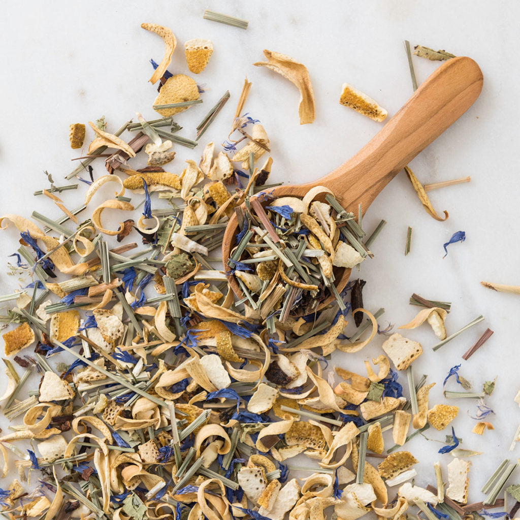 Assorted dried herbs and a wooden scoop on a white surface, Herbal Tea Calme N°2 by L'Infuseur – Honeybush & Verbena