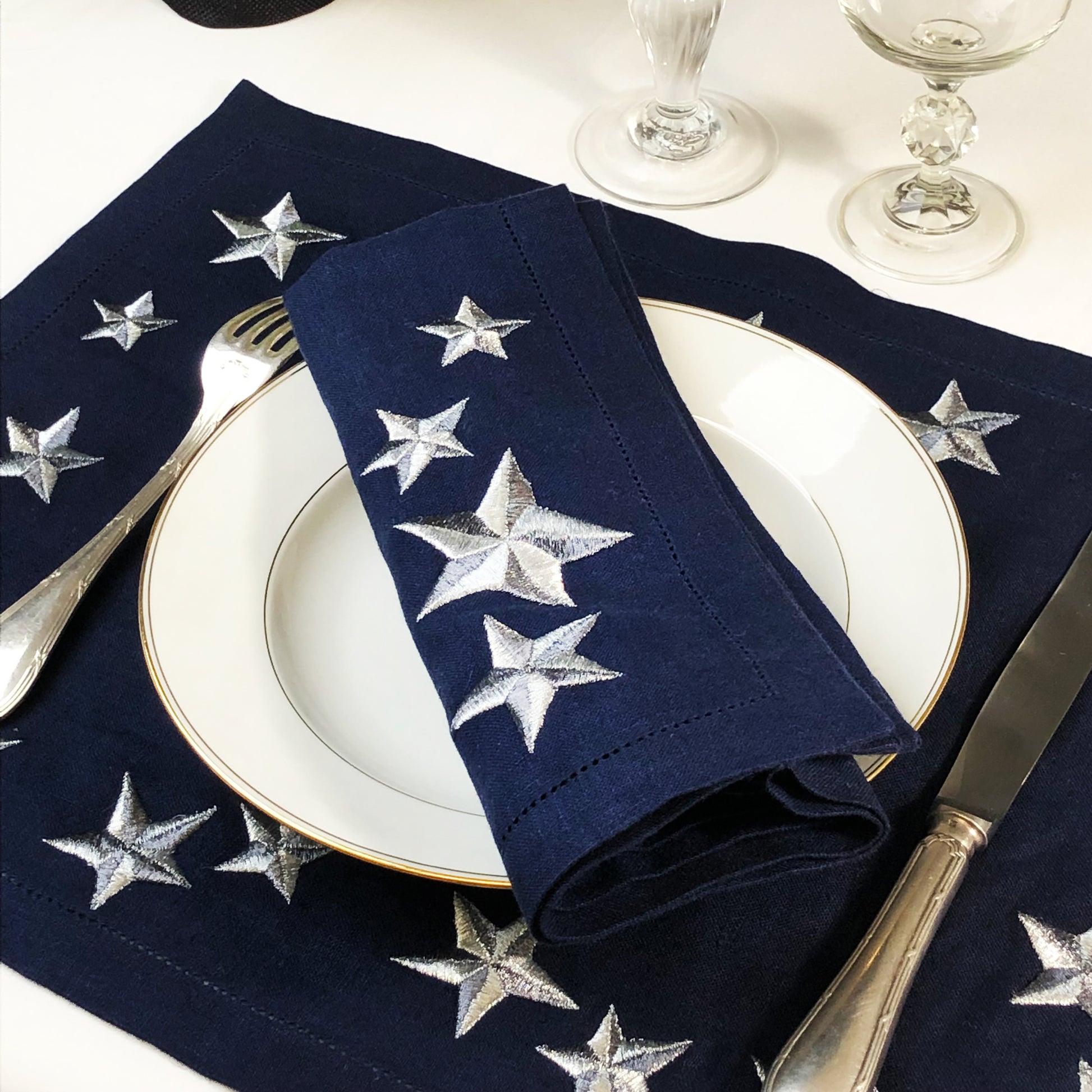 Napkins with star patterns on a table setting with plates and cutlery. Lucky Stars Linen Placemat – Hand Embroidered – Maison Holder

