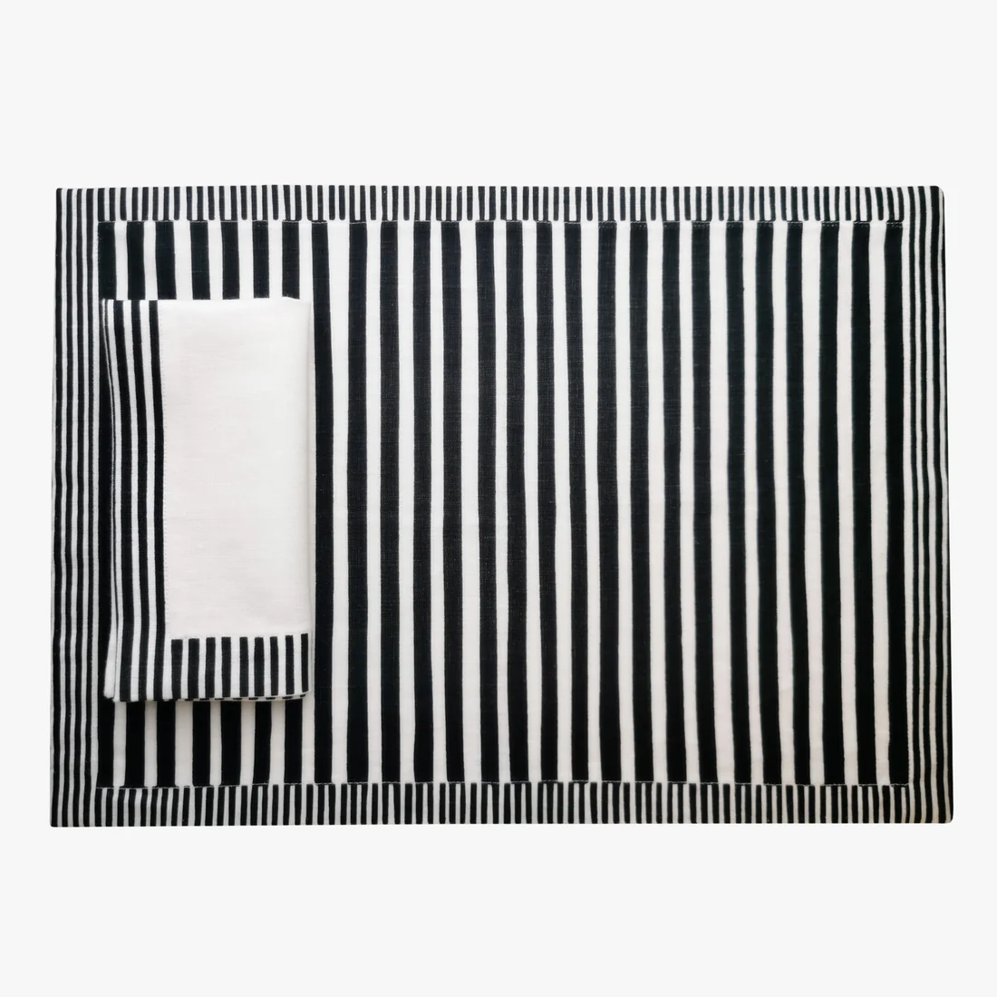 Black and white striped placemat with a folded white napkin on a white background, Milleraies Striped Linen Placemat – Aurelie Bidermann – Maison Holder