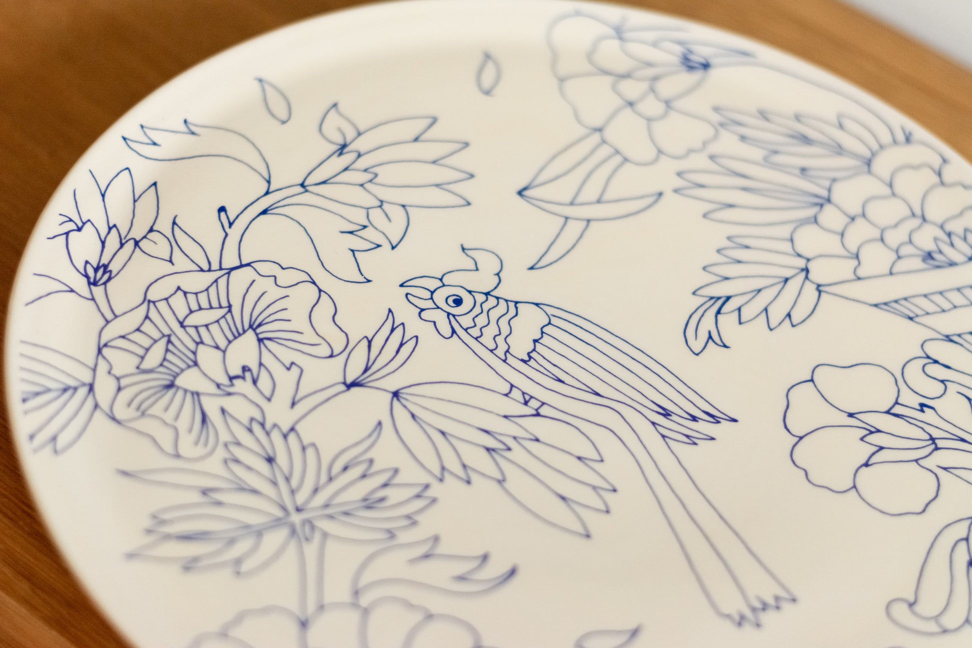 White plate with blue floral and bird designs on a wooden surface, Cake Platter Rouen Decor – Desvres Earthenware – Maison Holder