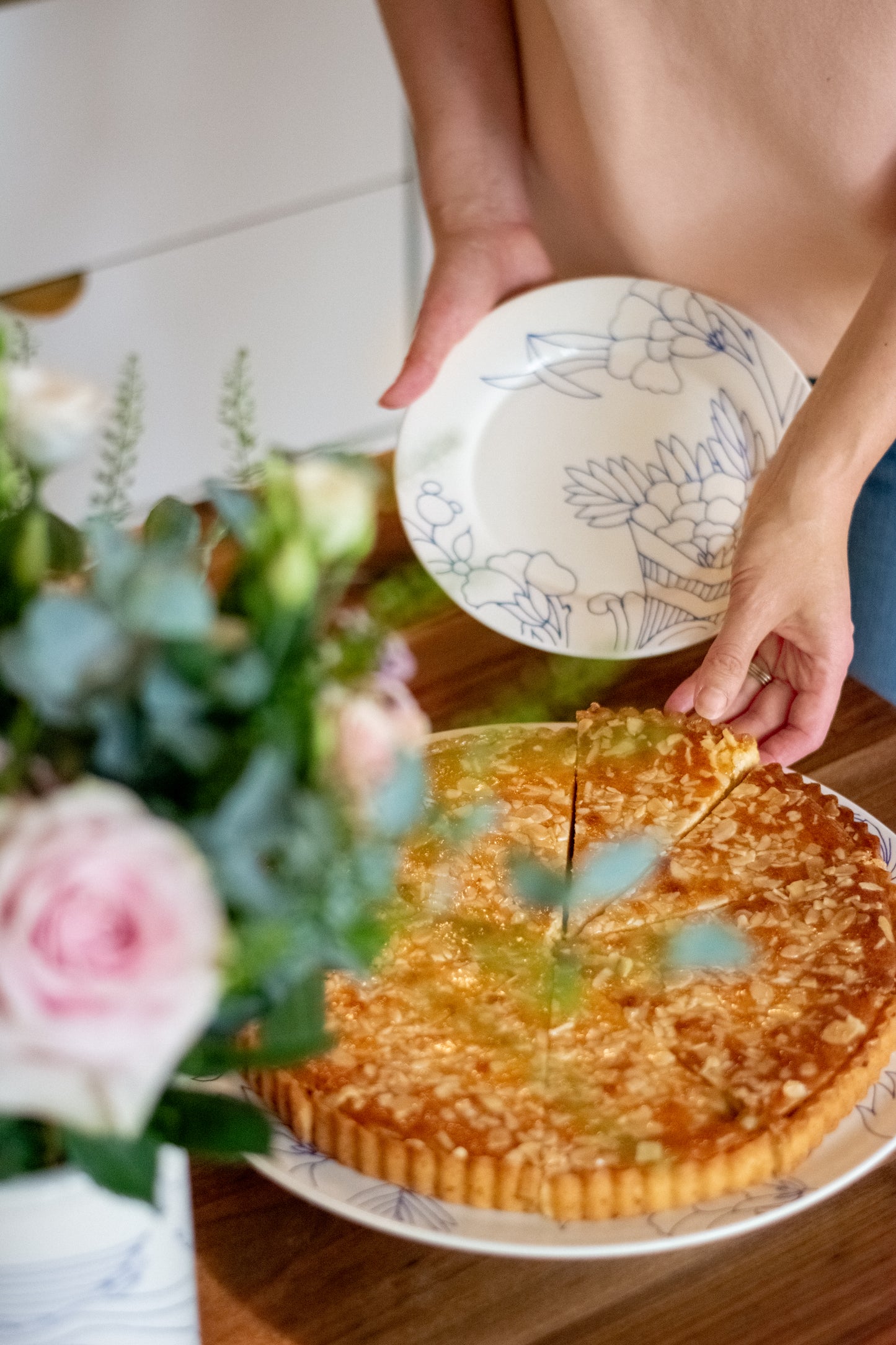 Person cutting a pie with a decorative plate on a wooden table, surrounded by flowers., Dessert Plate Rouen Decor – Desvres Earthenware – Maison Holder