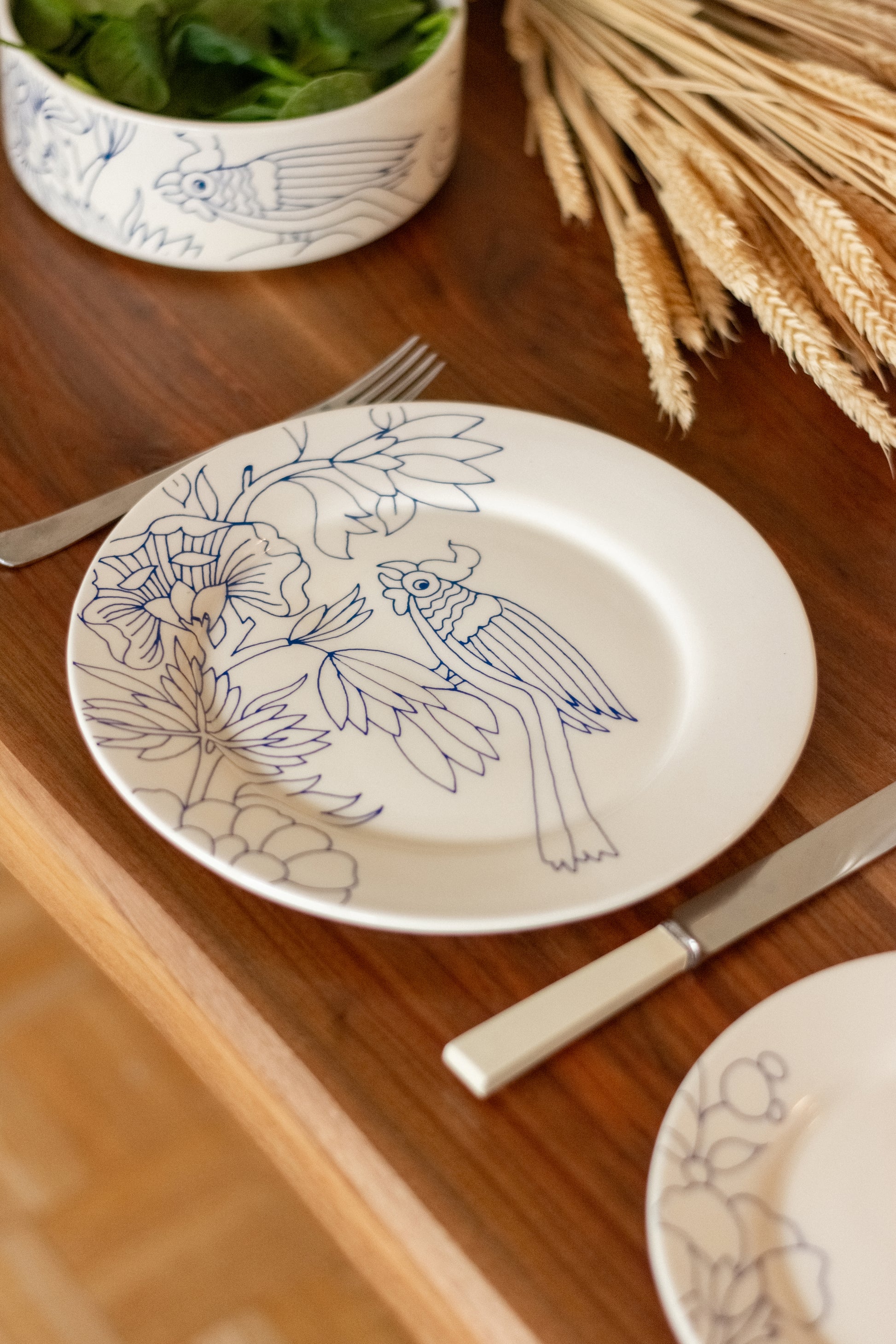 Decorative plate with bird and floral design on a wooden table with cutlery and a bowl. Dinner Plate Rouen Decor – Desvres Earthenware – Maison Holder
