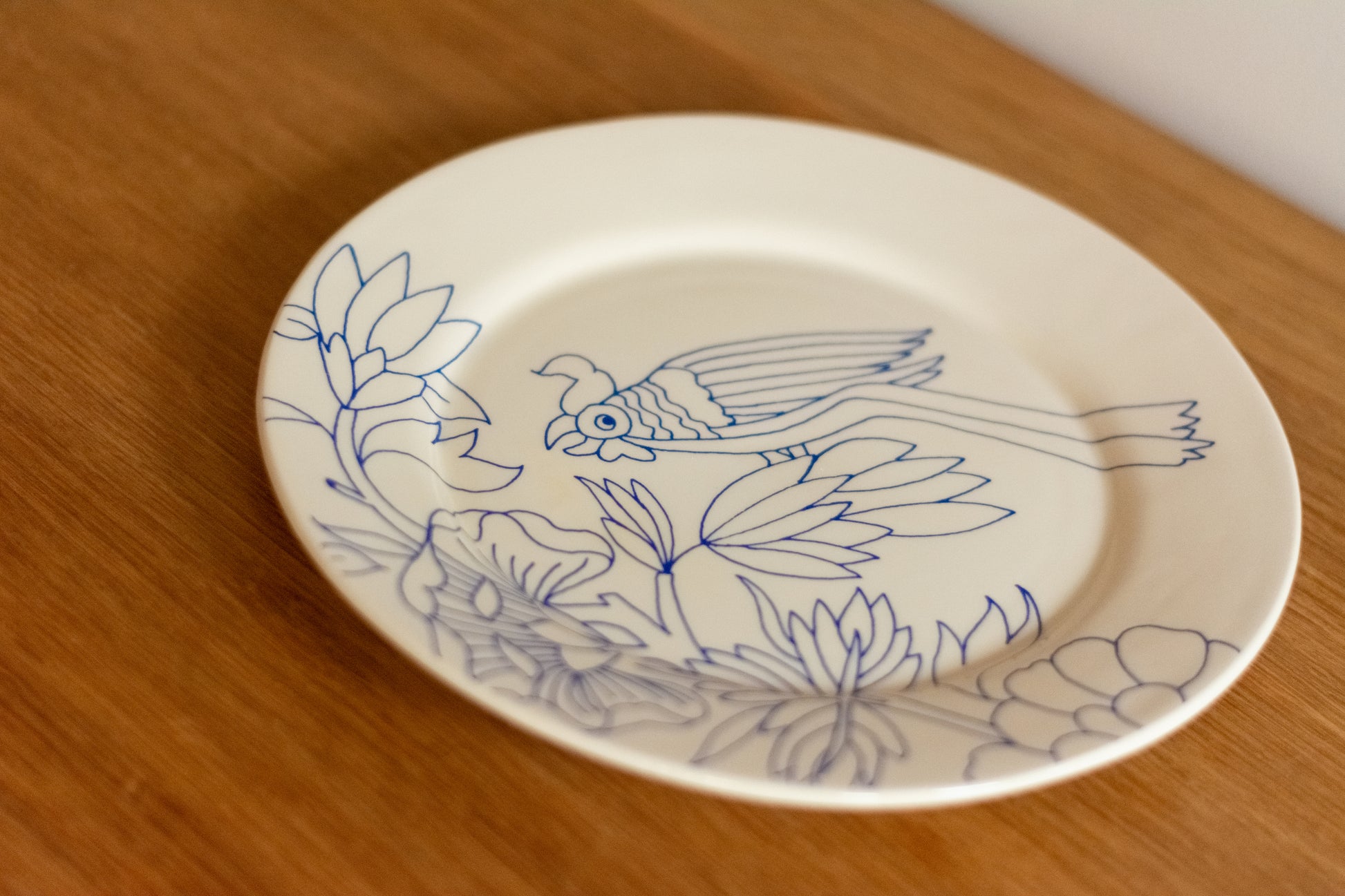 White plate with blue floral and bird design on a wooden surface, Dinner Plate Rouen Decor – Desvres Earthenware – Maison Holder