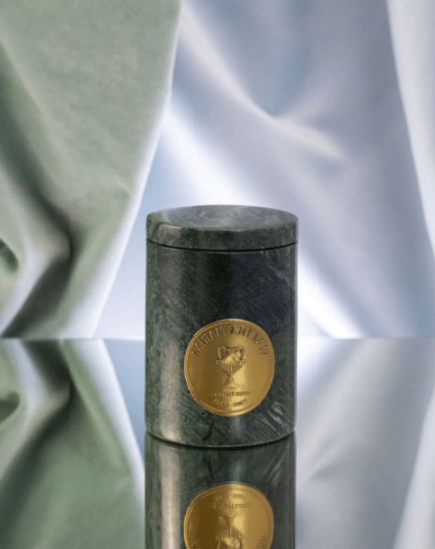 Marble cylindrical container with gold emblem on a reflective surface, Tindari Marble Candle – Venetico Marina – Maison Holder