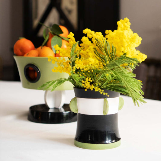 Bouquet of yellow flowers in a black and white striped vase on a table with oranges in the background., Calypso Black Table Vase by Olivier Gagnère – Ceramic Art – Maison Holder